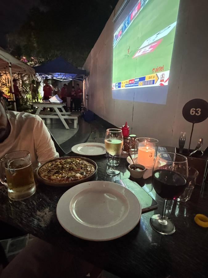 Pub table with pizza and drinks, football on a big screen
