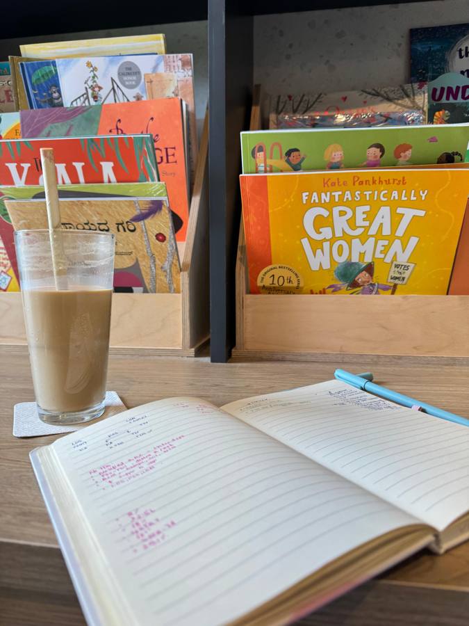Vanilla latte next to an open journal and a shelf of books
