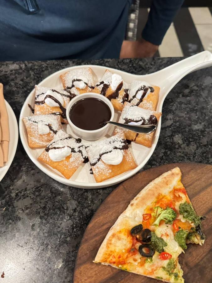 Sugar-dusted dough puffs with chocolate sauce next to a pizza slice