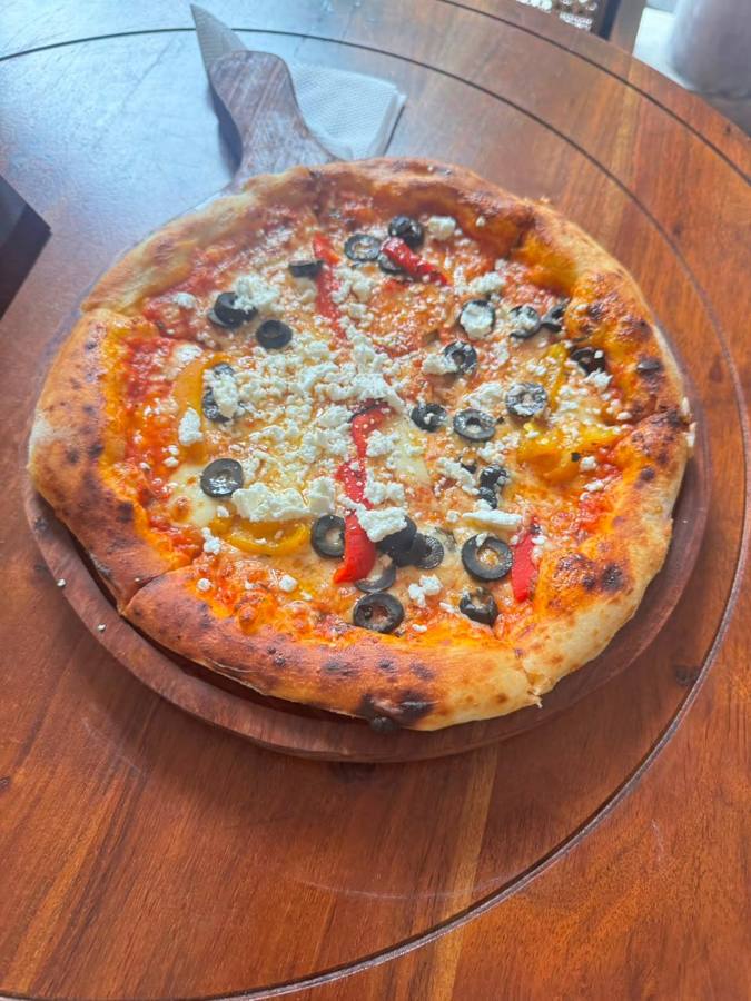 Pizza with olives, feta and peppers on a wooden board